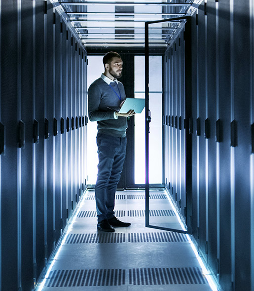A man with a laptop computer standing in a mainframe hallway.