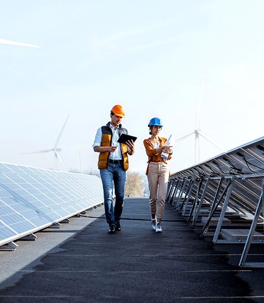 Professionals wearing hardhats, walking through a field of solar panel sheets. 