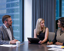 Three business people at a conference table talking to one another.