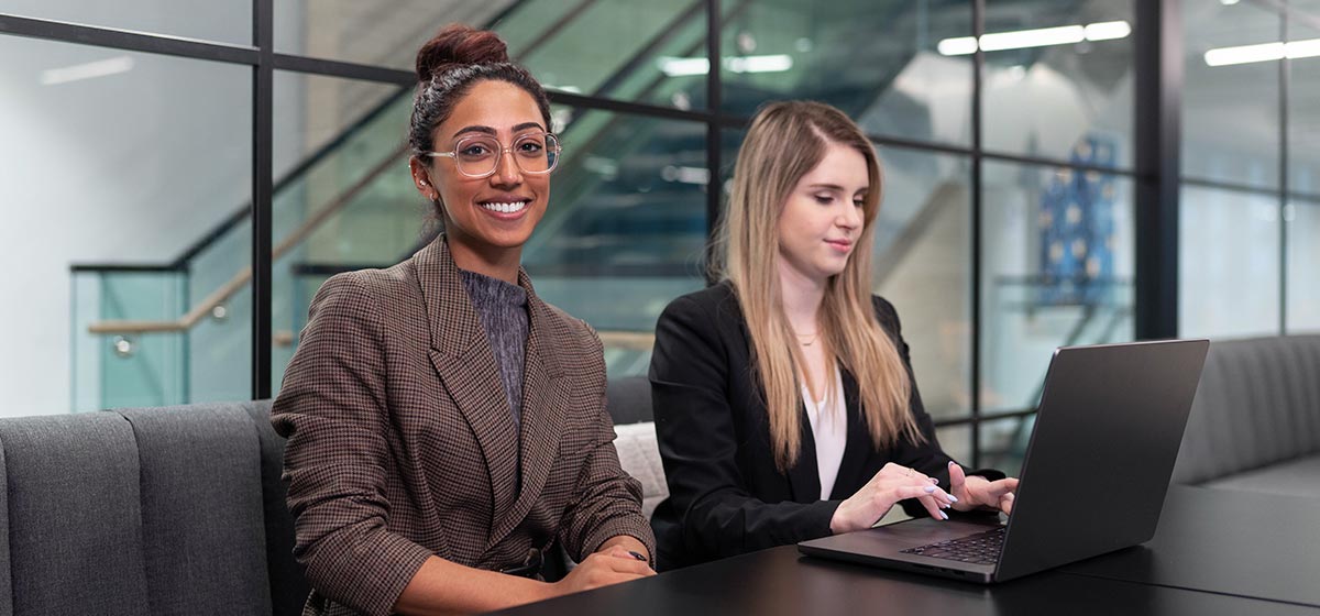 Two women dressed professionally at a conference table. One is smiling and looking towards the camera.