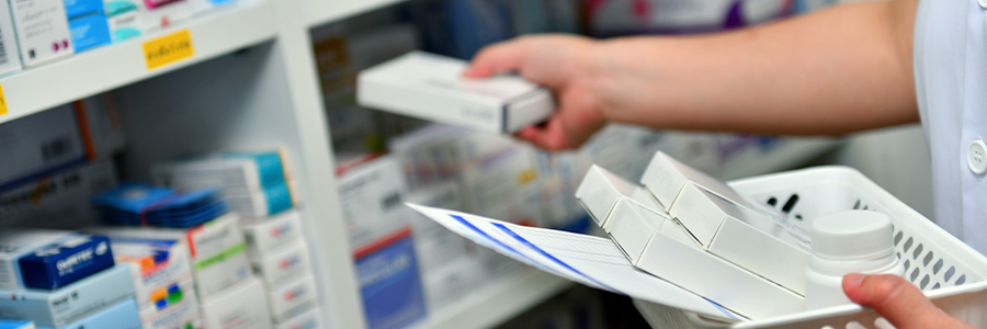 Close up of a pharmacist's hands collecting prescriptions from shelves of packaged drugs.