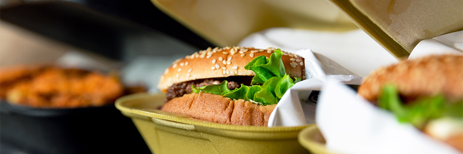 Gros plan d’un hamburger et d’autres produits de restauration rapide dans des contenants à emporter.