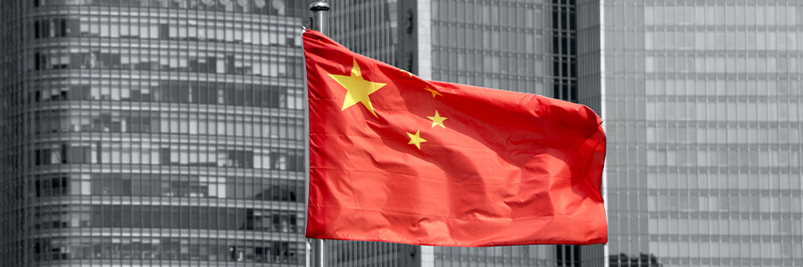 The Chinese flag flying at the top of a flagpole with office buildings in the background