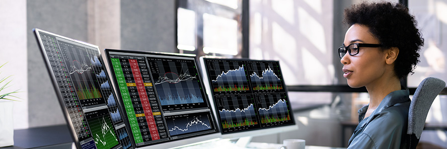 A woman at a desk surrounded by computer monitors displaying chart data.