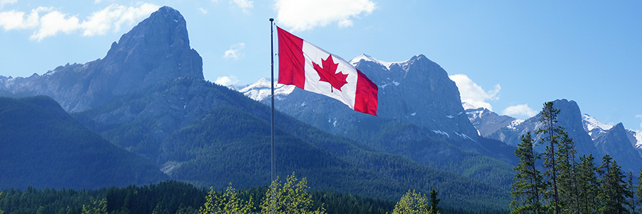 Un drapeau canadien flottant au vent avec les montagnes Rocheuses canadiennes en arrière-plan.