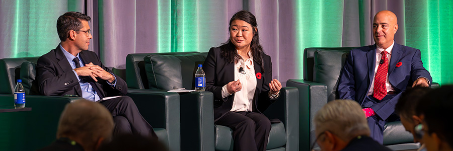 Guest speakers sitting in chairs on-stage engaged in conversation.