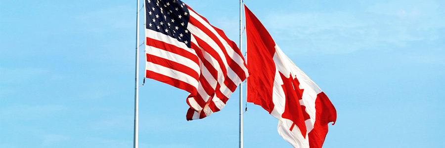 Two flagpoles. One is flying the American flag while the second is flying the Canadian flag.