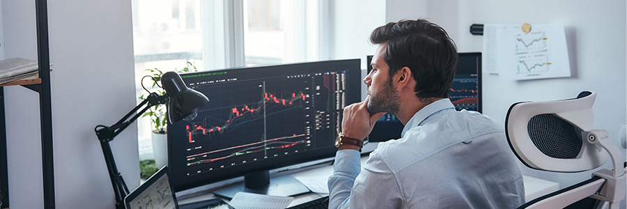 A man sitting at a desk with multiple computer monitors displaying data on large charts.