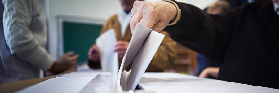 A ballot box with a voter inserting a folded piece of paper.