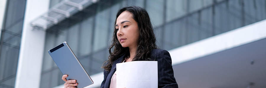 A businessperson holding printouts and looking at information on a tablet computer.