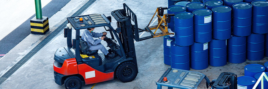 A forklift in a warehouse moving oil barrels.