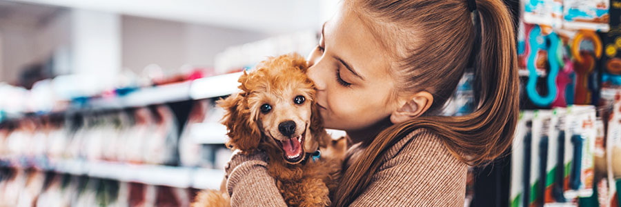 Une fille dans un magasin de fournitures pour animaux de compagnie qui tient un chien dans ses bras.