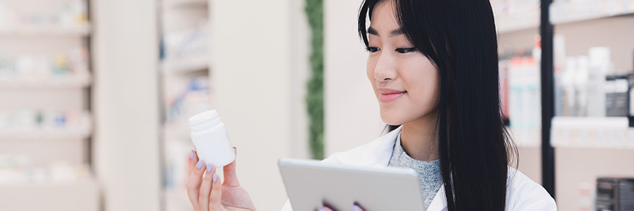 A pharmacist holding a tablet computer and looking at a bottle of prescription medicine.