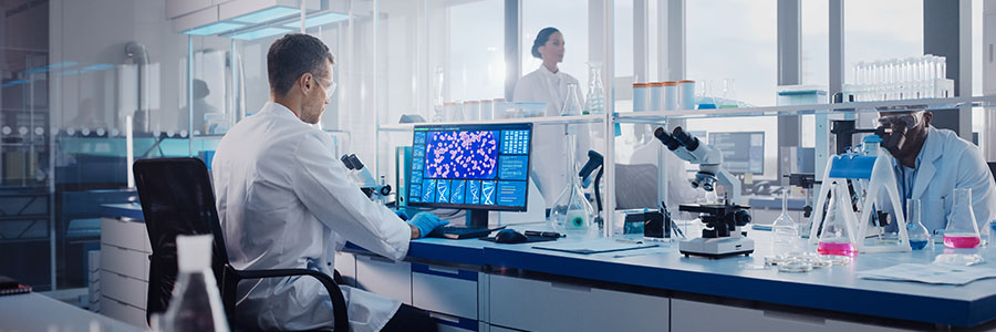 Biotech lab technicians studying test results on a computer and in a microscope.