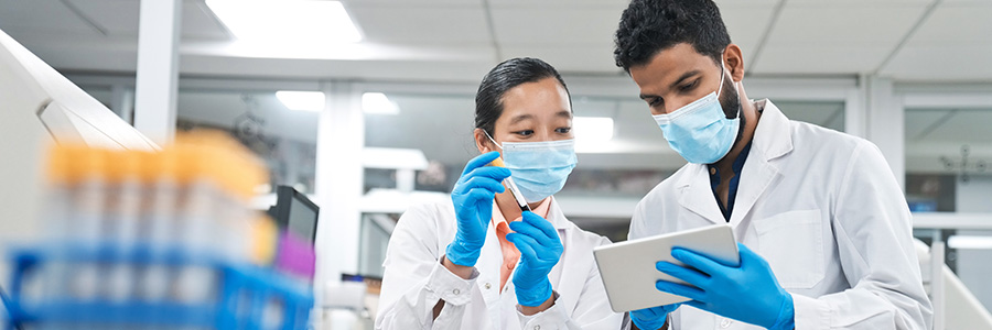 A lab technician holding a blood sample in a test tube and a second lab technician using a tablet computer.