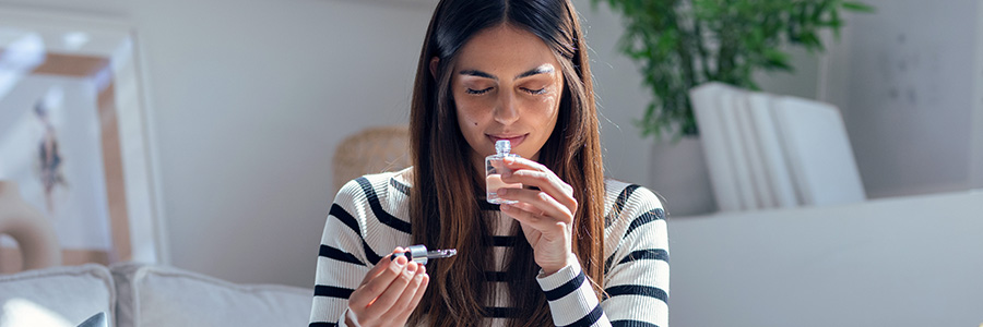 A woman with her eyes closed sniffing an open perfume bottle.