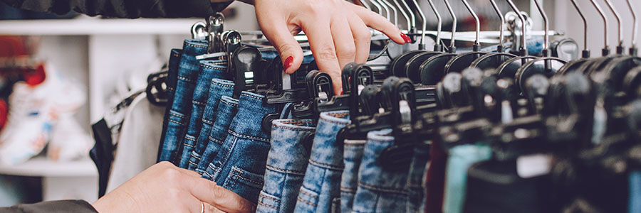 Gros plan de mains qui trient des jeans sur des cintres dans le présentoir d’un magasin.