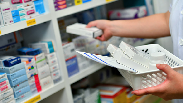 Close up of a pharmacist's hands collecting prescriptions from shelves of packaged drugs.