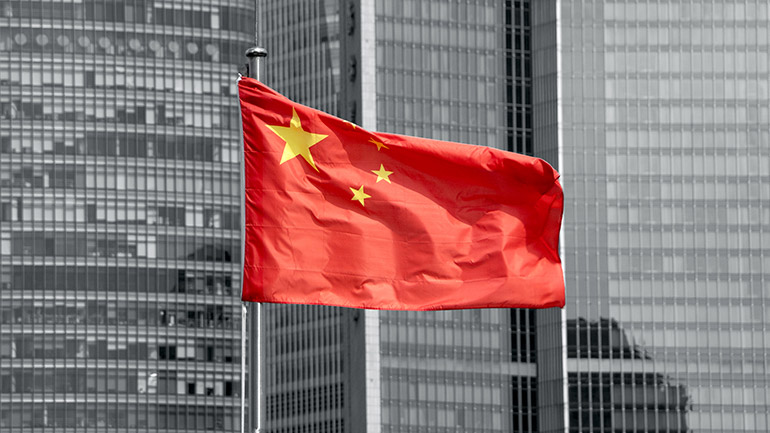 The Chinese flag flying at the top of a flagpole with office buildings in the background.