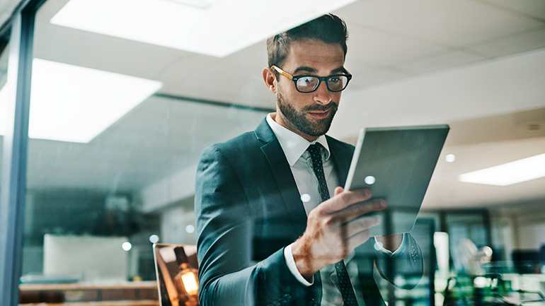 A businessperson in an office setting looking at information on a tablet computer.