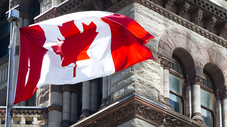 A Canadian flag flying in the wind in front of the Parliament buildings in Ottawa.