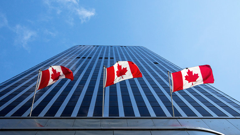 Trois drapeaux canadiens devant une grande tour de bureaux vus d’en bas.