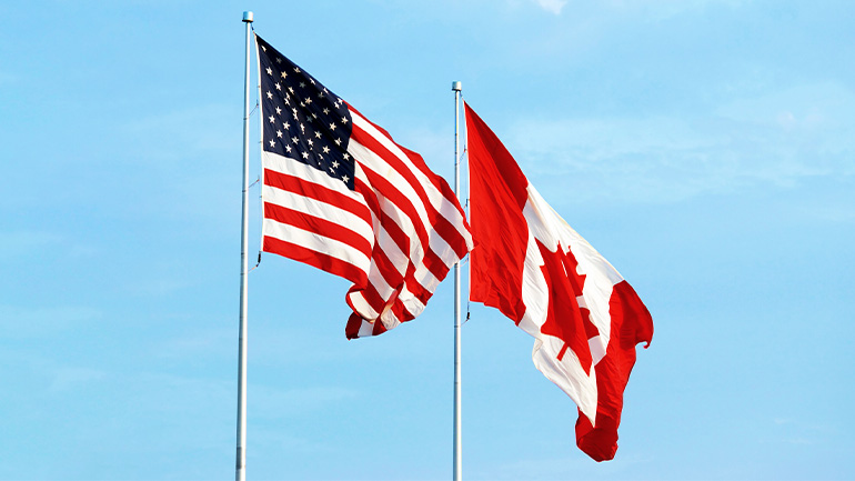 Two flagpoles. One is flying the American flag while the second is flying the Canadian flag.