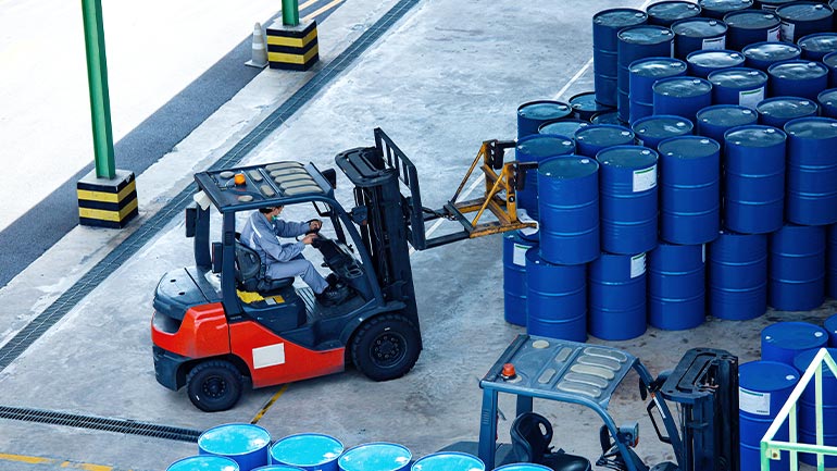 A forklift in a warehouse moving oil barrels.