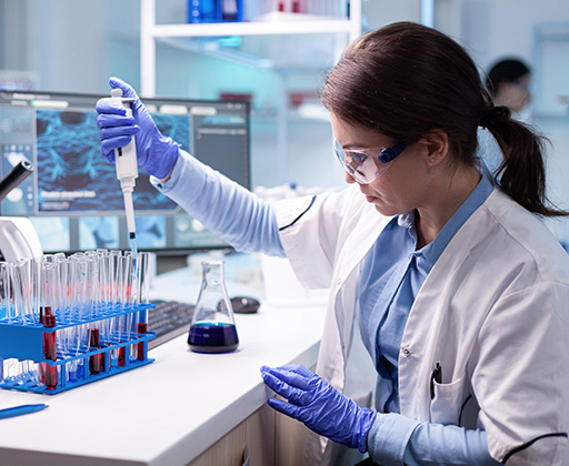 A woman in lab clothes uses a micropipette to fill test tubes.