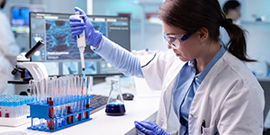 A woman in lab clothes uses a micropipette to fill test tubes.